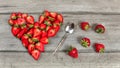 Top down view, strawberry pieces arranged in shape of heart, spoon and some spilled strawberries near, on gray wood desk