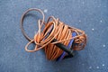 Top down view, tangled orange power cord extension lead on blue roll, over dirty carpet.