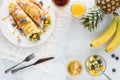 Top down view of tropical fruit crepes on a white plate surrounded by various breakfast foods. Royalty Free Stock Photo