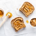 Top down view of two slices of multigrain toast topped with creamy peanut butter and honey.