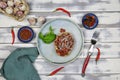 Top down view on white wood table, dish with basil tomato pecorino cheese bread, garlic bulbs, red raw chillies, fork, blue cloth
