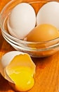 glass bowl with two, white, eggs, one brown egg and a cracked open white, egg shell Royalty Free Stock Photo