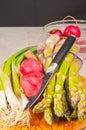 Two local, ripe, radish, bundle of asparagus, four green onions and pairing knife, on a rare wood plate