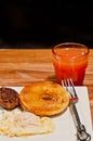 Fried egg, sausage paddy, half of a toasted bangle, artisan fork on square, white plate with a glass of grapefruit juice