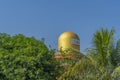 Top of a golden color Lord Shiva Lingam temple in Puttaparthi with green trees