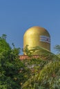 Top of a golden color Lord Shiva Lingam temple in Puttaparthi with green trees