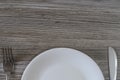 Top half of white empty plate, knife and fork on grey wooden tab