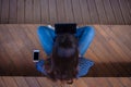 The top of the head is a brunette student girl with sitting cross-legged, on a bench, with open laptop, typing.