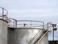 Top of large old silver steel industrial storage tanks with control valves rusting stairs and walkway against a blue sky Royalty Free Stock Photo