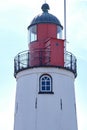Top of a lighthouse against a blue sky. Red and black metal, window with bars. Background Royalty Free Stock Photo
