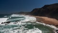 Top ocean coast view with sandy beach, black rocks, blue sky and huge waves Royalty Free Stock Photo