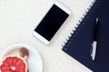 Top of the office desk with smartphone blue notebook pen and plate with spoon and grapefruit Royalty Free Stock Photo