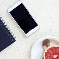 Top of the office desk with smartphone blue notebook pen and plate with spoon and grapefruit Royalty Free Stock Photo