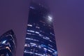 upper part of modern glass skyscrapers shrouded in fog. Night view of commercial building on th background of glowing purple sky Royalty Free Stock Photo