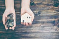 Top perspective view of right hand holding money coins and left hand holding house model on top of wood table. Concept of mortgage