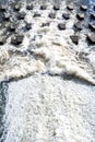 Top perspective view to flow of foaming water crashing on small concrete stones-breakwaters. Royalty Free Stock Photo