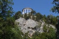 On the top of a rocky hill is an architectural construction of a circular shape with columns of white against the