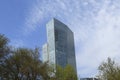 The top of tall beautiful modern elegant glass skyscraper above the trees against blue sky and white clouds. Esentai Tower, Almaty Royalty Free Stock Photo