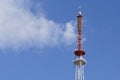 The top of a tall television tower against a blue sky and white cloud. Telecommunications, radio and communications Royalty Free Stock Photo