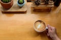 Top up view of hand holding coffee cup on brown wooden table with cactus pot, coppy space for text