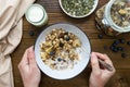 Top vie of hand holding spoon of oats for breakfast, granola with dried fruit and blueberry, milk and honey. Wooden background.