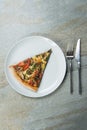 Top viev of Slice of veggie pizza on plate. Knife and fork near the dish on stone anthracite background.