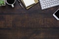 Top view above of dark old wooden office desk table with keyboard, notebook and coffee cup with equipment other office supplies. Royalty Free Stock Photo