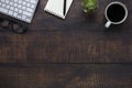 Top view above of dark old wooden office desk table with keyboard, notebook and coffee cup with equipment other office supplies. Royalty Free Stock Photo