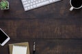 Top view above of dark wood office desk table with keyboard, notebook and coffee cup with equipment other office supplies.