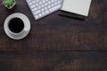 Top view above of Dark wooden office desk table with keyboard, notebook and coffee cup with equipment other office supplies. Royalty Free Stock Photo