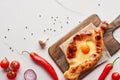 Top view of adjarian khachapuri on cutting board with vegetables on marble texture.