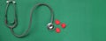 Image of a top view stethoscope and red heart on a green background, concept of health and medicine.