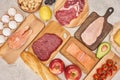 Top view af raw organic assorted meat, poultry, fish, eggs, apples, lemon, avocado, tomatoes and peanuts on wooden