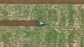 Top view of an agricultural tractor crossing a field right down the center, from left to right, tilling a field creating furrows