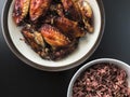 Top view of air fried chicken wings on ceramic dish serve with small bowl of cooked Rice berry. All on black background. Royalty Free Stock Photo