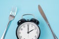 Top view alarm clock with knife and fork on blue background. Intermittent fasting, Ketogenic dieting, weight loss, meal plan and Royalty Free Stock Photo