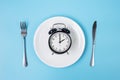 Top view alarm clock on white plate with knife and fork on blue background. Intermittent fasting, Ketogenic dieting, weight loss, Royalty Free Stock Photo