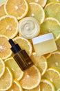 Top view of an amber dropper bottle, yellow cream jar places on surface of orange slices.