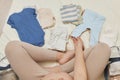 Top view of anonymous pregnant woman carefully selecting clothing for the newborn while preparing for maternity hospital expecting Royalty Free Stock Photo