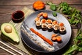 Top view of appetizing Japanese sushi rolls in big black plate, serving with fish slices, sauces, caviar, avocado, salad Royalty Free Stock Photo