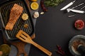 top view of arranged grilled salmon steak on wooden cutting board, ingredients, sauce and cutlery on black tabletop Royalty Free Stock Photo