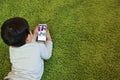 Top view of asian cute and smart little boy lying on geen floor while using or playing game from cell phone device with attention Royalty Free Stock Photo