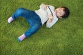 Top view of asian cute and smart little boy lying on geen floor while using or playing game from cell phone device with attention Royalty Free Stock Photo