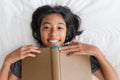 Top view of asian girl holding book brown while lying in bed, Asia little girl smile and looking at camera