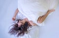 Top view of attractive, young, sexy, dark-haired woman, windblown hair wild on the sheets, mouth open, laughing, one leg kicked Royalty Free Stock Photo