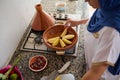 Top view Muslim woman in hijab, standing by stove on kitchen counter and stacking potato slices in a tagine clay pot