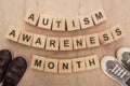 Top view of autism awareness month words made of wooden blocks near brown and grey children sneakers.