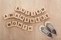 Top view of autism awareness month words made of wooden blocks near grey children sneakers.