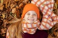 Top view of awesome teenage girl child wearing vinous sweater, orange hat, scarf, lying on yellow fallen maple leaves.