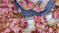 Top view baby girl seating on ground covered in pink petals, in stripy tights, blue skirt and silver shoes, holding camelia flower Royalty Free Stock Photo